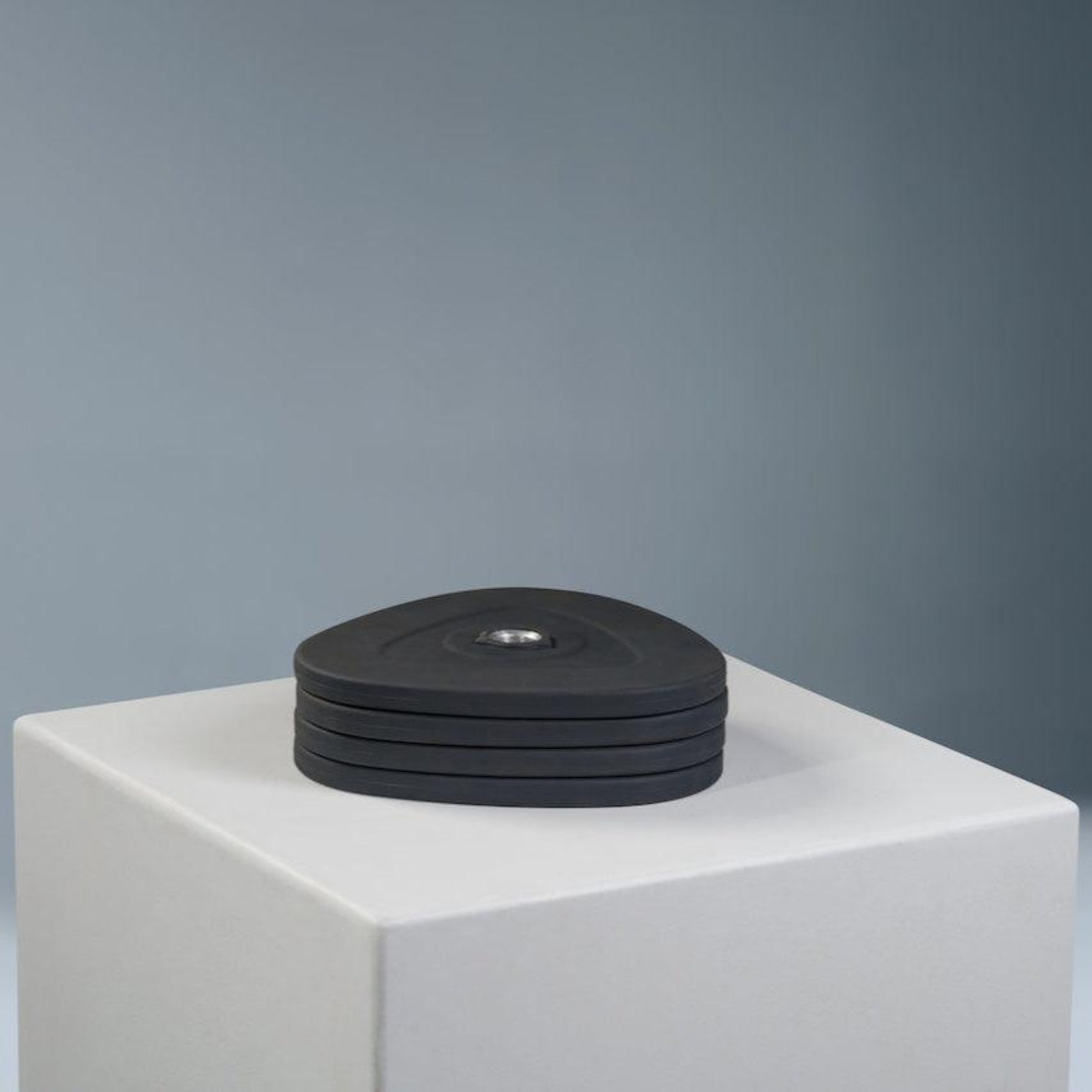 A set of black dumbbell weight plates on a white pedestal against a grey background.