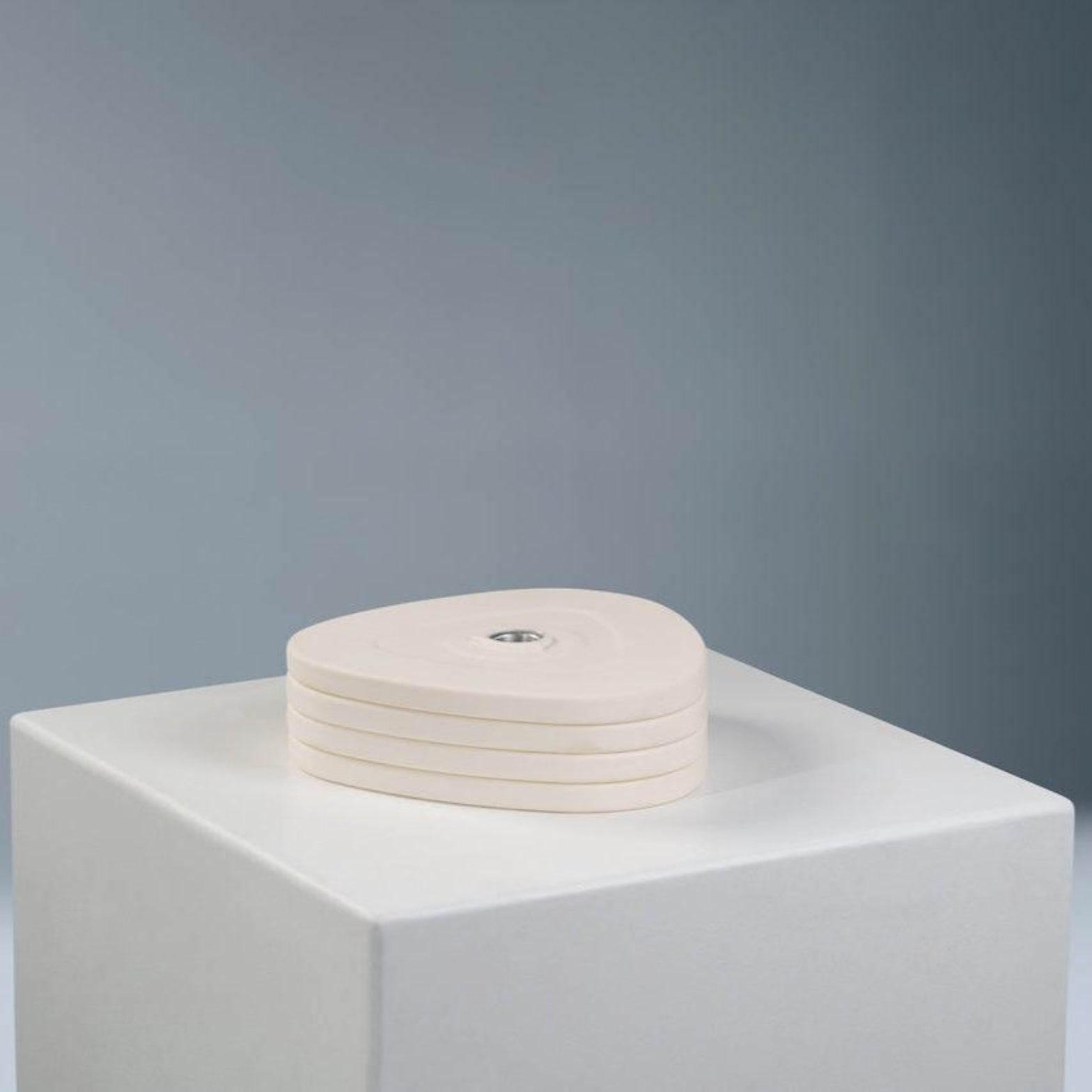A set of white dumbbell weight plates on a white pedestal against a grey background.